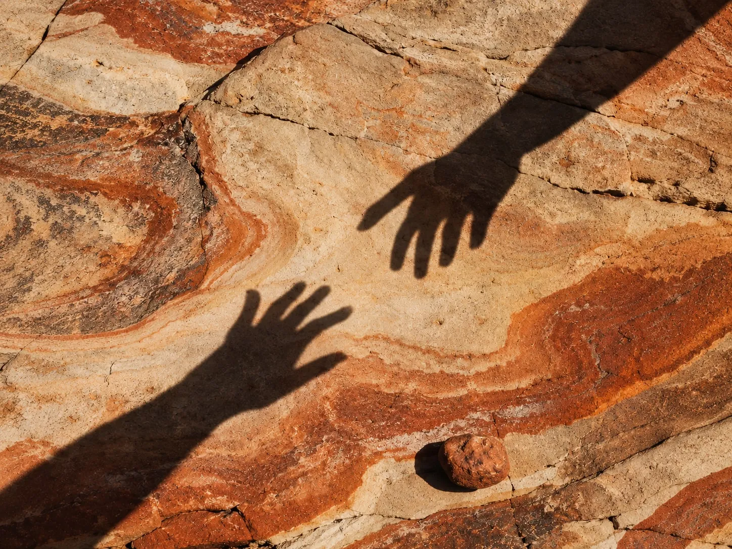 Two hand shadows reaching toward each other across banded ochre sandstone