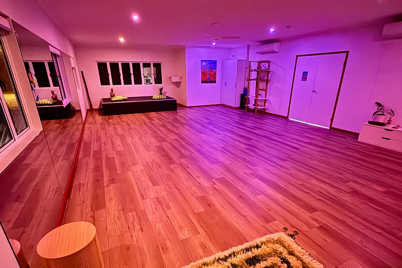 The studio at night under pink and violet light: the timber floor running to the far windows and the double doors.